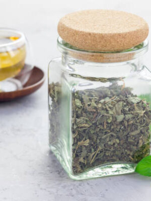 Dry herbal mint tea in a jar with cup of tea on background, horizontal